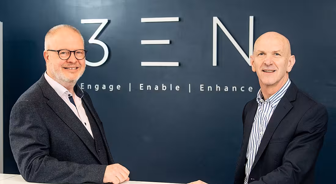 Two men in suits are standing in front of a 3EN-branded wall and smiling into the camera.
