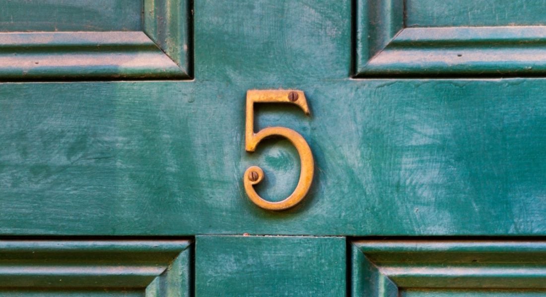A number 5 in bronze on an old wooden green door.
