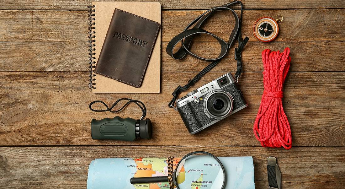 A wooden table with survival camping equipment including a map, camera, passport and more.