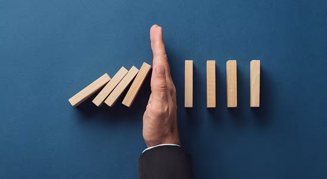 Top view of business person stopping falling dominos from collapsing on a navy blue background.
