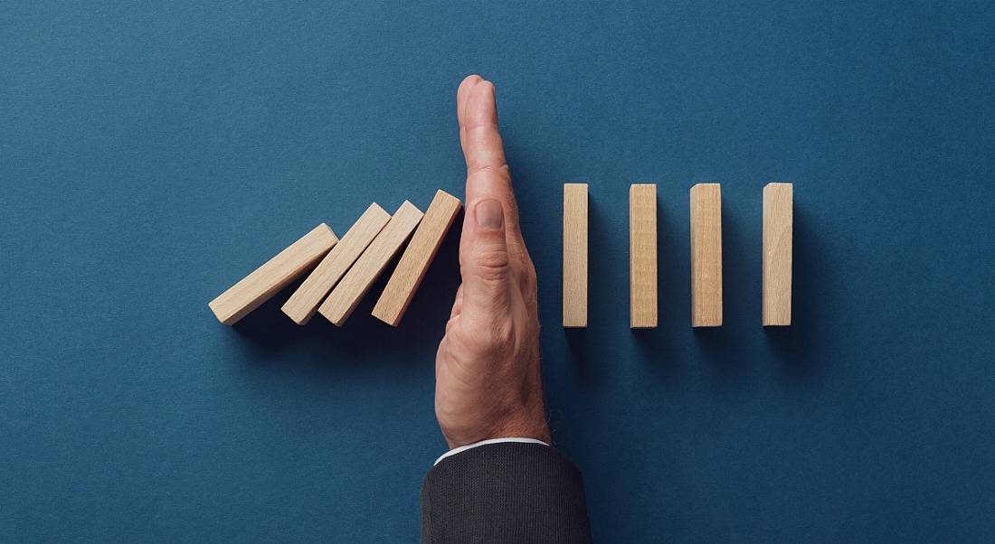 Top view of business person stopping falling dominos from collapsing on a navy blue background.