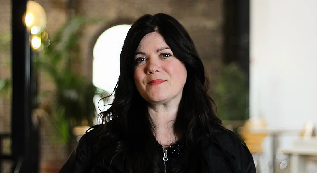 A head and shoulders shot of a woman with long dark hair. She is Aileen Carville, talking about her fashion tech career.