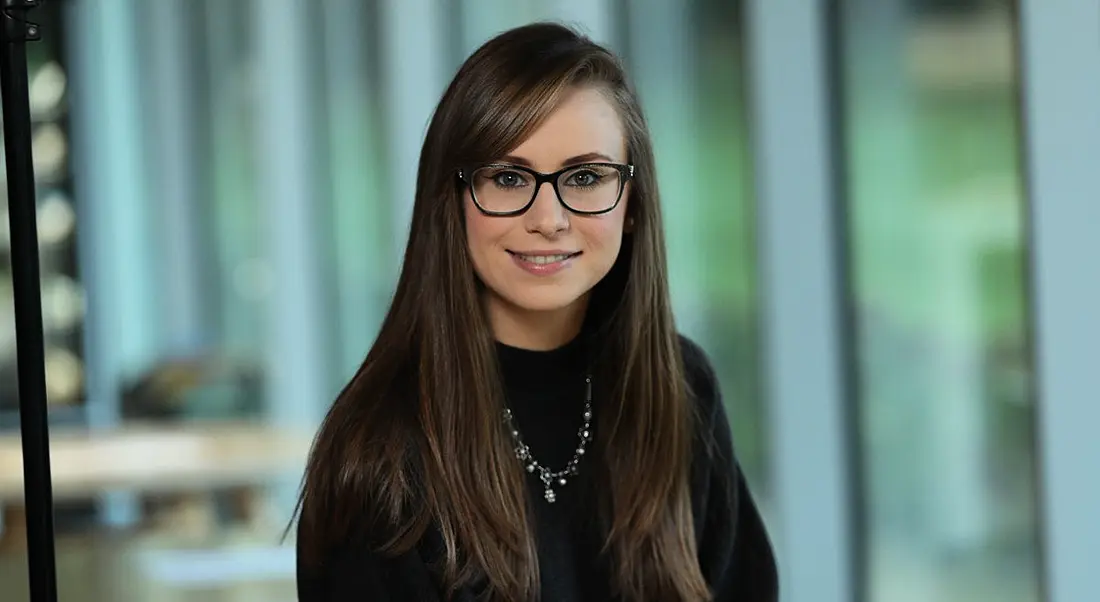 Software developer at Fidelity Investments, Elaine Healy, is smiling into the camera in an office.