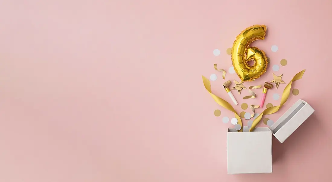 Number 6 birthday balloon popping out of a box, against pale pink background.