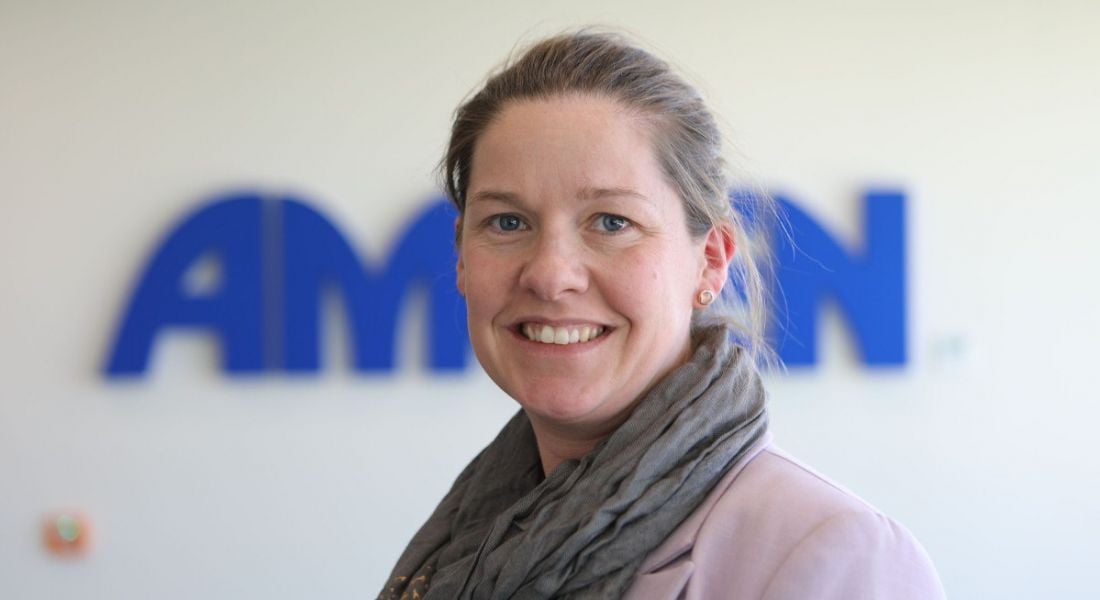 Michelle Somers is smiling into the camera in front of a wall with an Amgen sign.