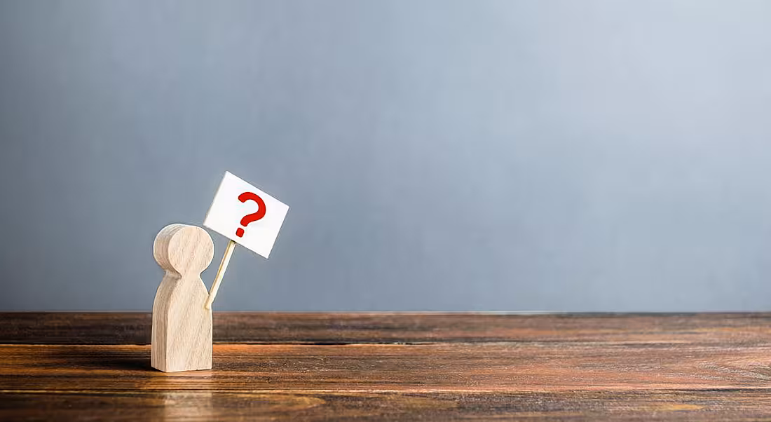 A small wooden figurine is holding a poster with a question mark on it.