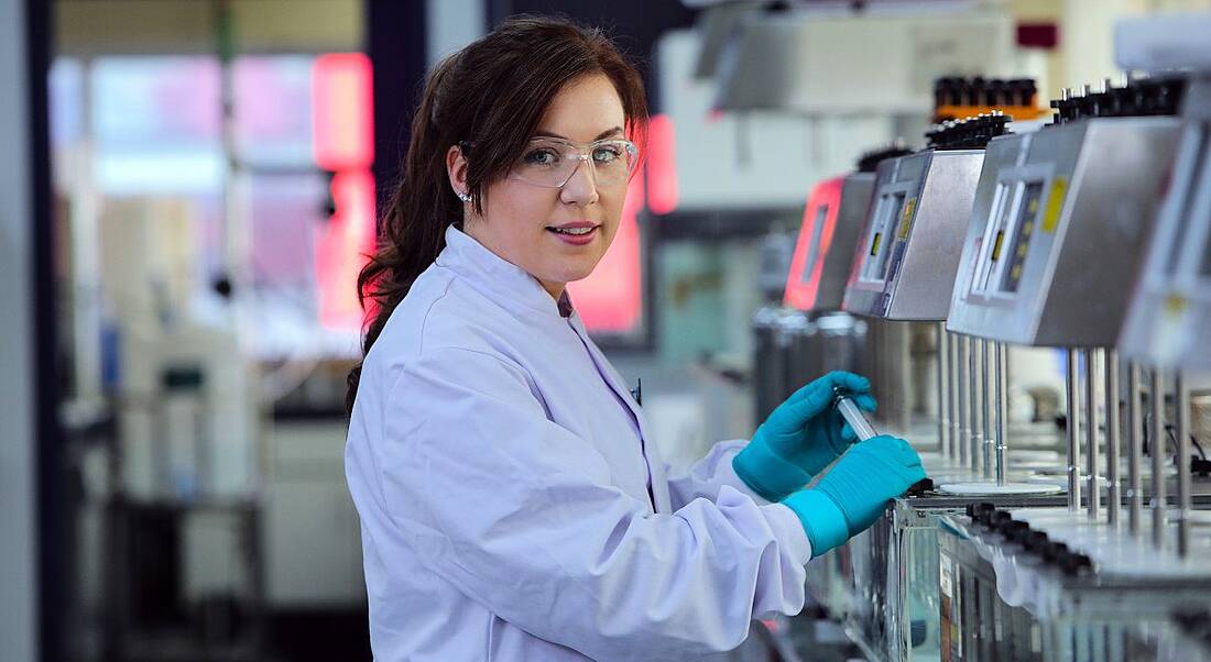 A woman is working in a lab at a station and looking into the camera.