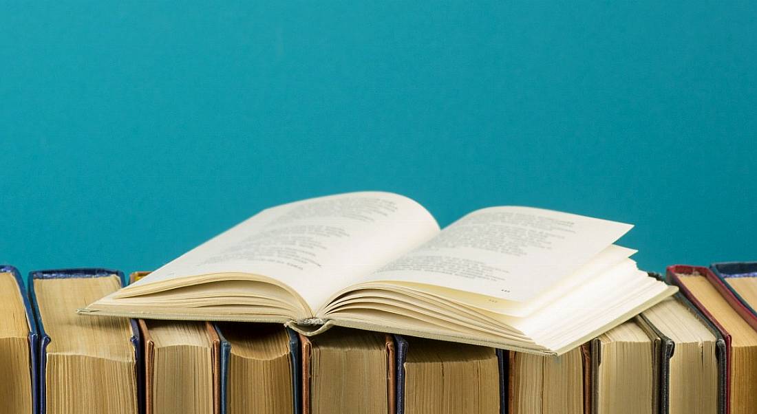 A row of books with one lying on top, sitting against a blue background.