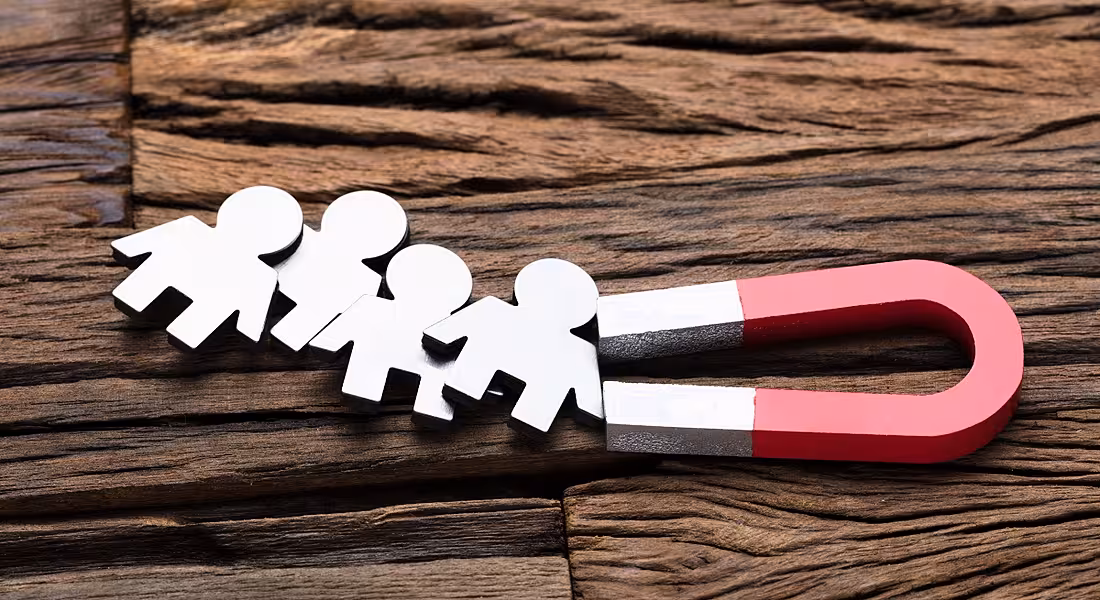 High angle view of magnet attracting people on wooden table, symbolising recruitment.