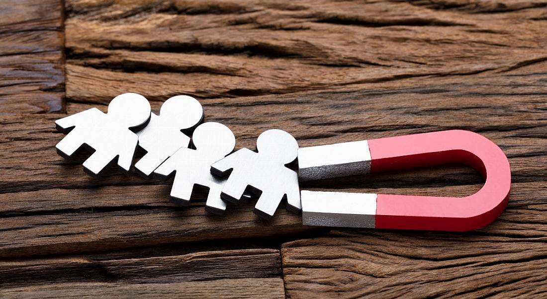 High angle view of magnet attracting people on wooden table, symbolising recruitment.