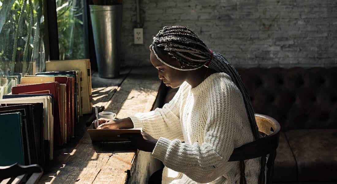 A woman is sitting in an empty cafe and reading a book, symbolising social distancing.