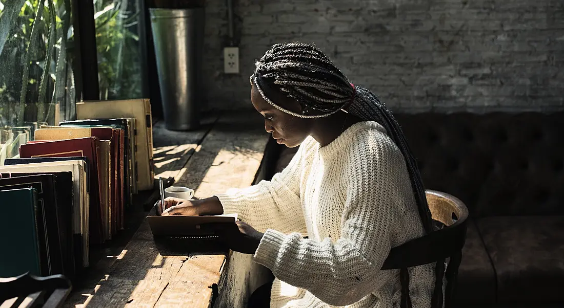 A woman is sitting in an empty cafe and reading a book, symbolising social distancing.