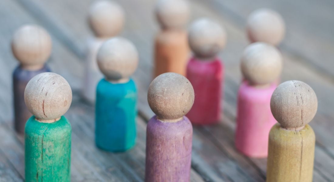 Wooden figures with different coloured bodies on a wooden table, representing diversity and inclusion.