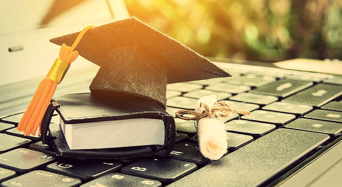 Black graduation cap, leather notebook and diploma on a laptop, symbolising software graduates.