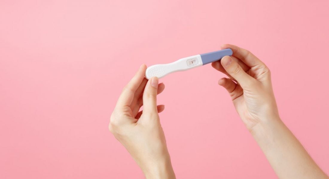A close-up of hands holding a pregnancy test against a bright pink background.