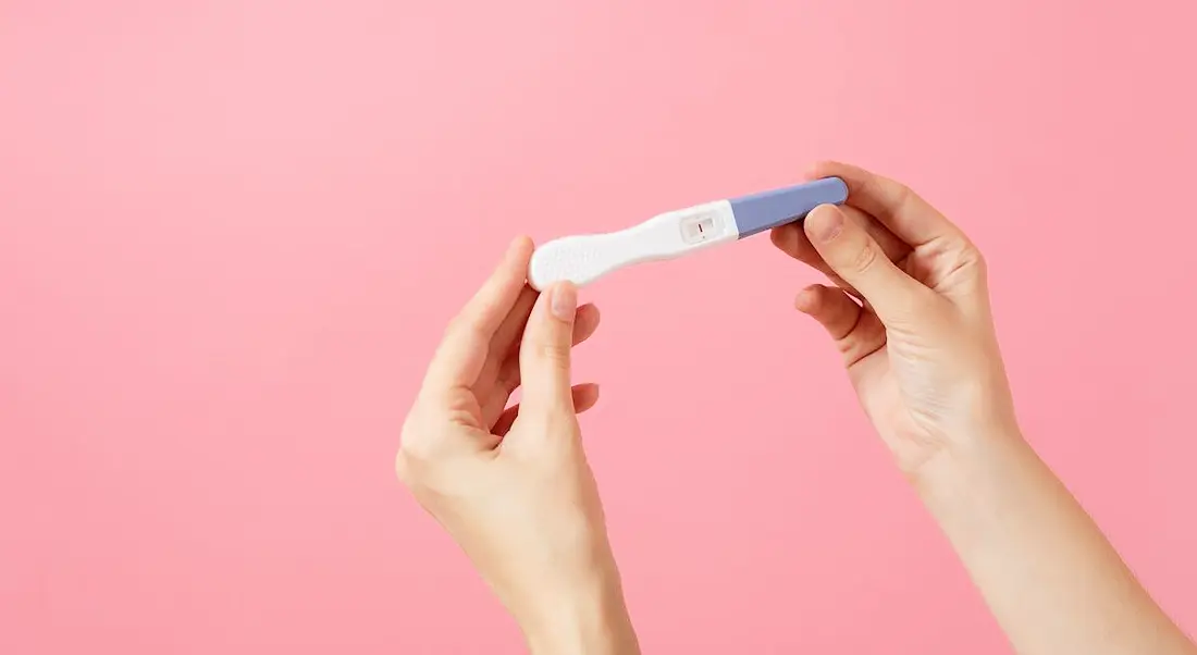 A close-up of hands holding a pregnancy test against a bright pink background.