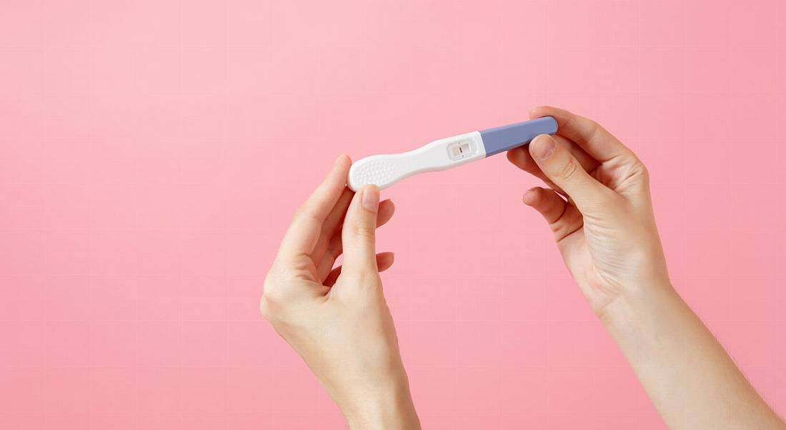 A close-up of hands holding a pregnancy test against a bright pink background.