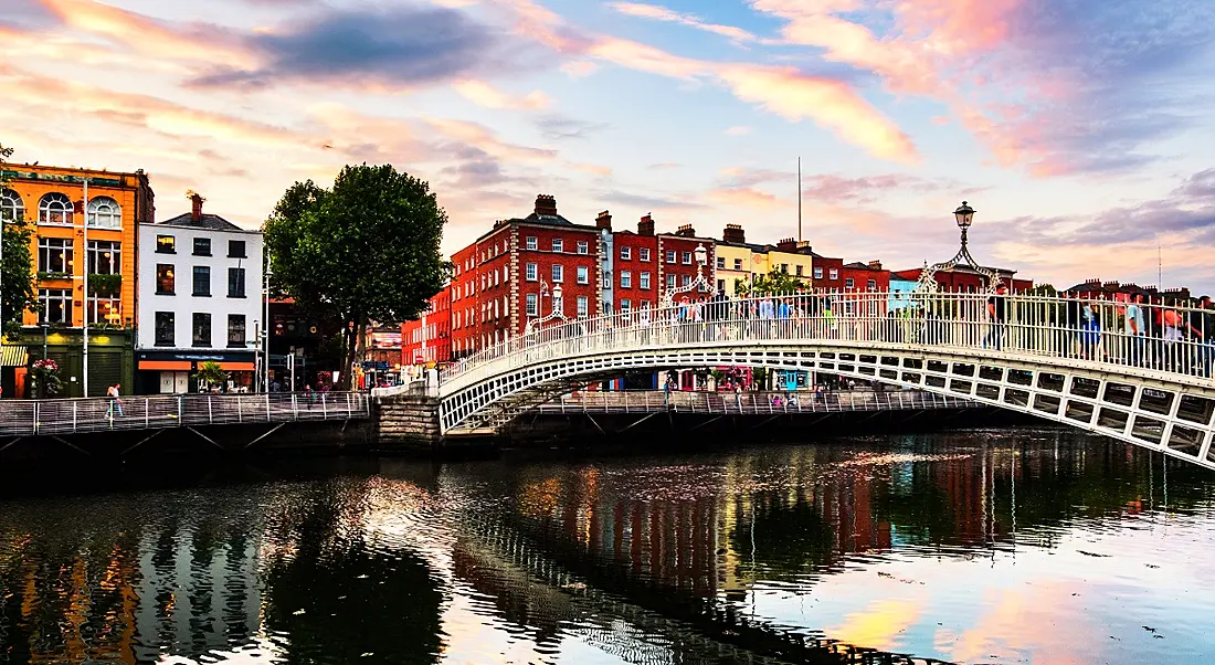 Photo of Ha'penny Bridge in Dublin, Ireland against a bright sky.