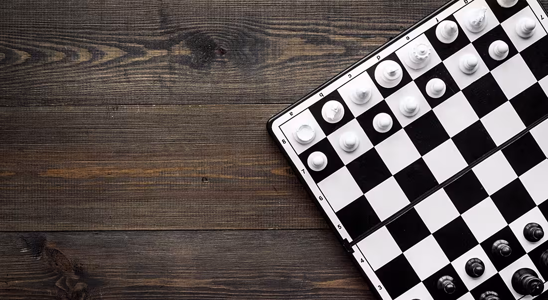 Top-down view of a black and white game of chess on a dark wooden table, symbolising game-based learning.