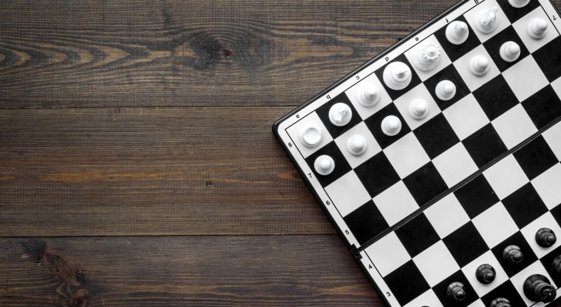 Top-down view of a black and white game of chess on a dark wooden table, symbolising game-based learning.