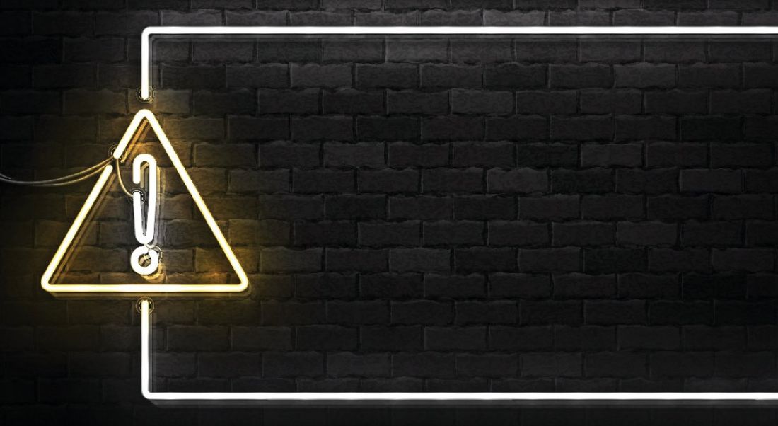 A lit up warning sign against a black brick background.