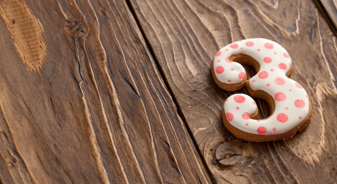 A number three-shaped biscuit with icing is lying on a wooden table.
