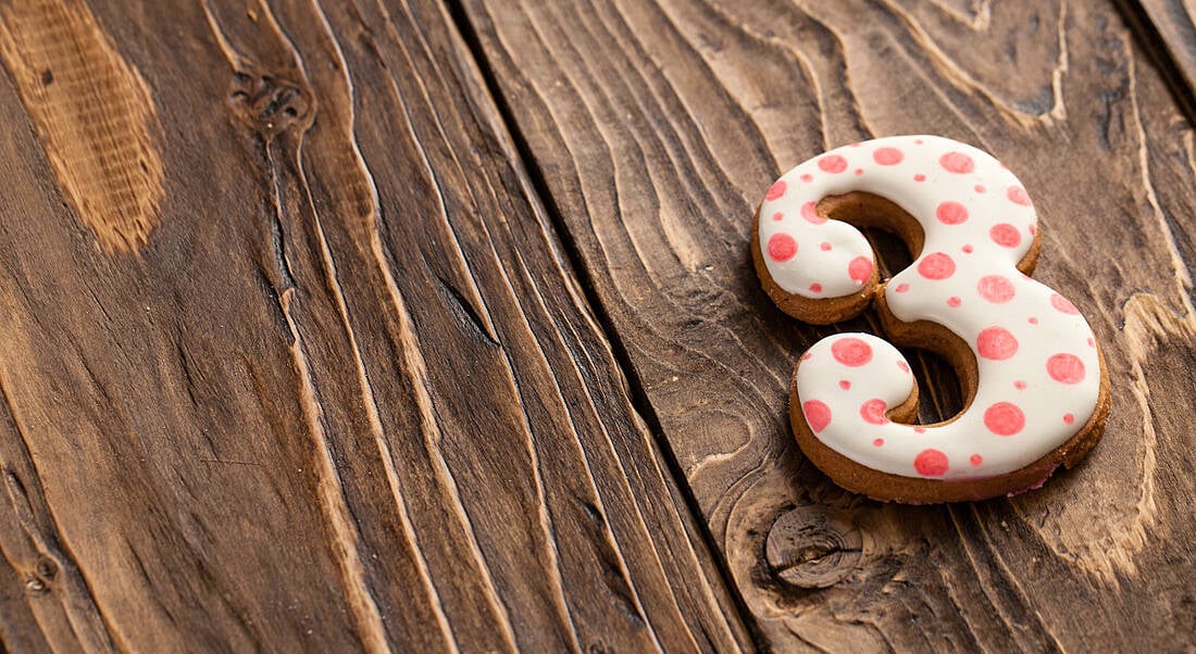 A number three-shaped biscuit with icing is lying on a wooden table.