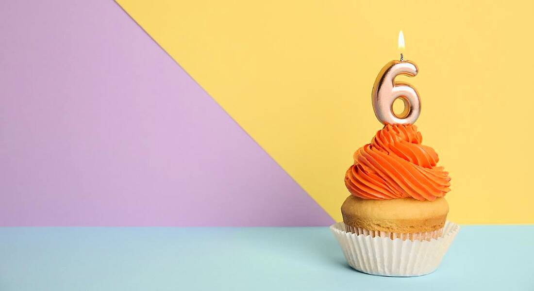 Birthday cupcake with number six candle on a yellow, purple and blue background.