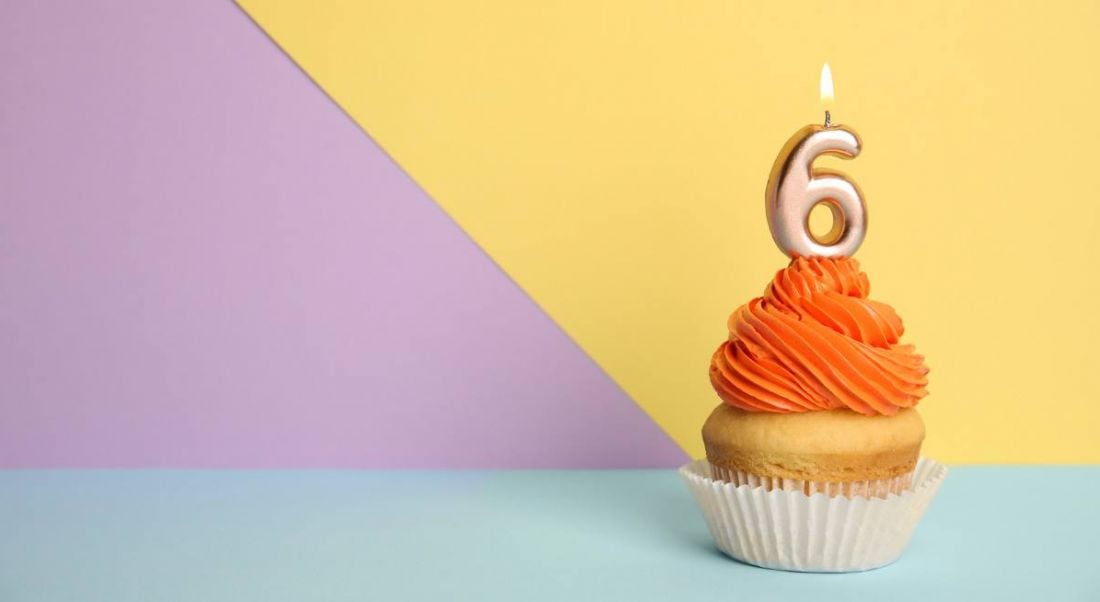 Birthday cupcake with number six candle on a yellow, purple and blue background.