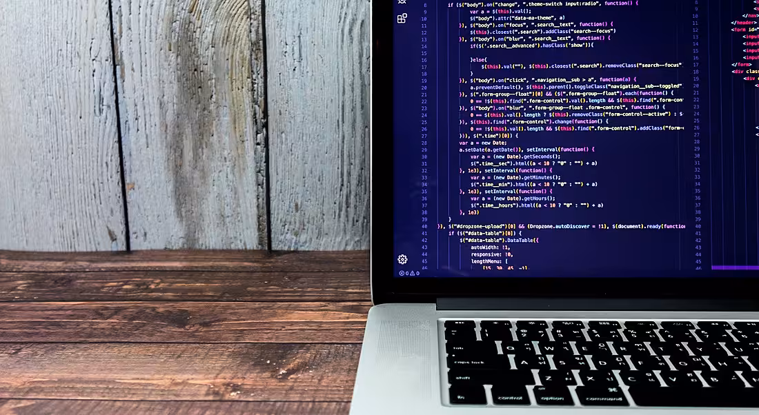 Lines of code on a laptop on top of a wooden desk.
