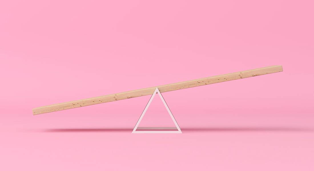 A wooden seesaw is balancing against a pink background, symbolising work-life balance.