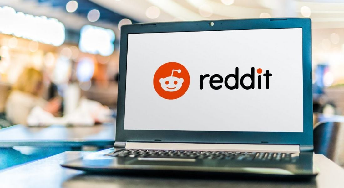 A laptop on a desk in an office with the Reddit logo on its screen.