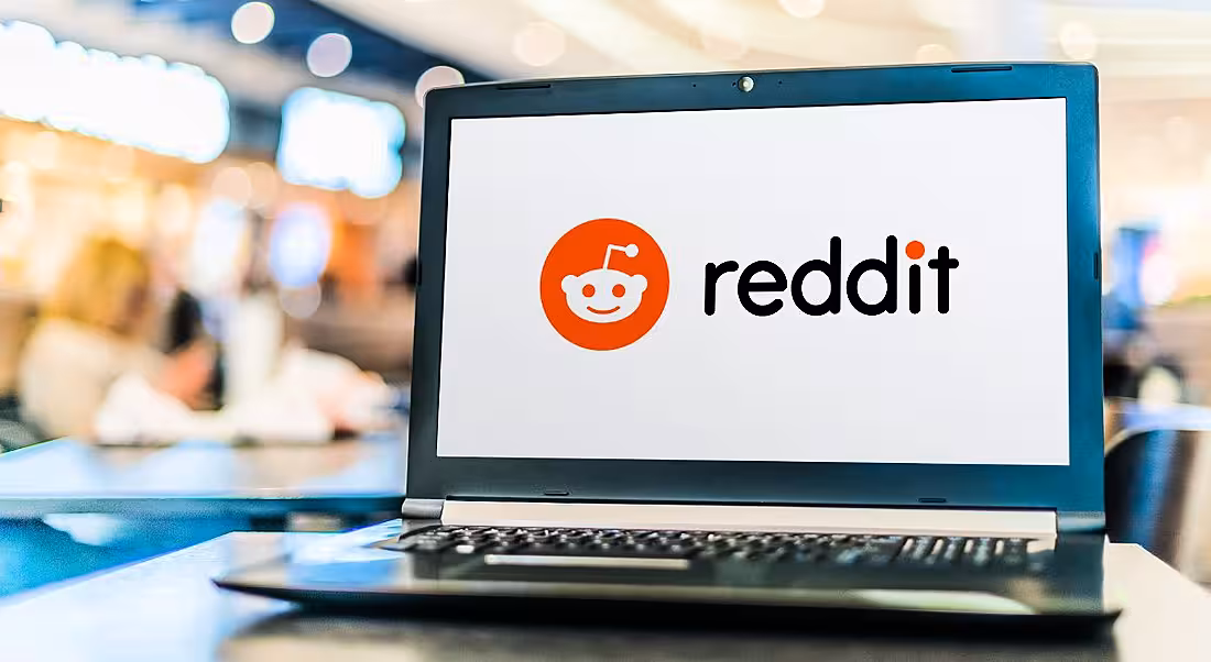A laptop on a desk in an office with the Reddit logo on its screen.