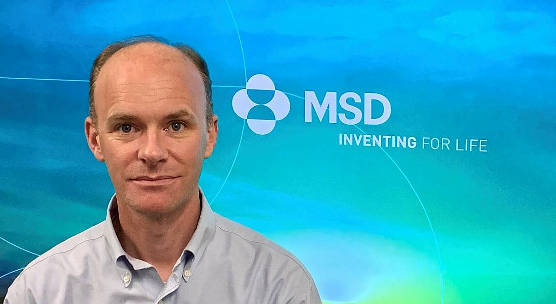 Barry Kennedy, automation engineer at MSD, is smiling into the camera in front of a screen with the company logo.