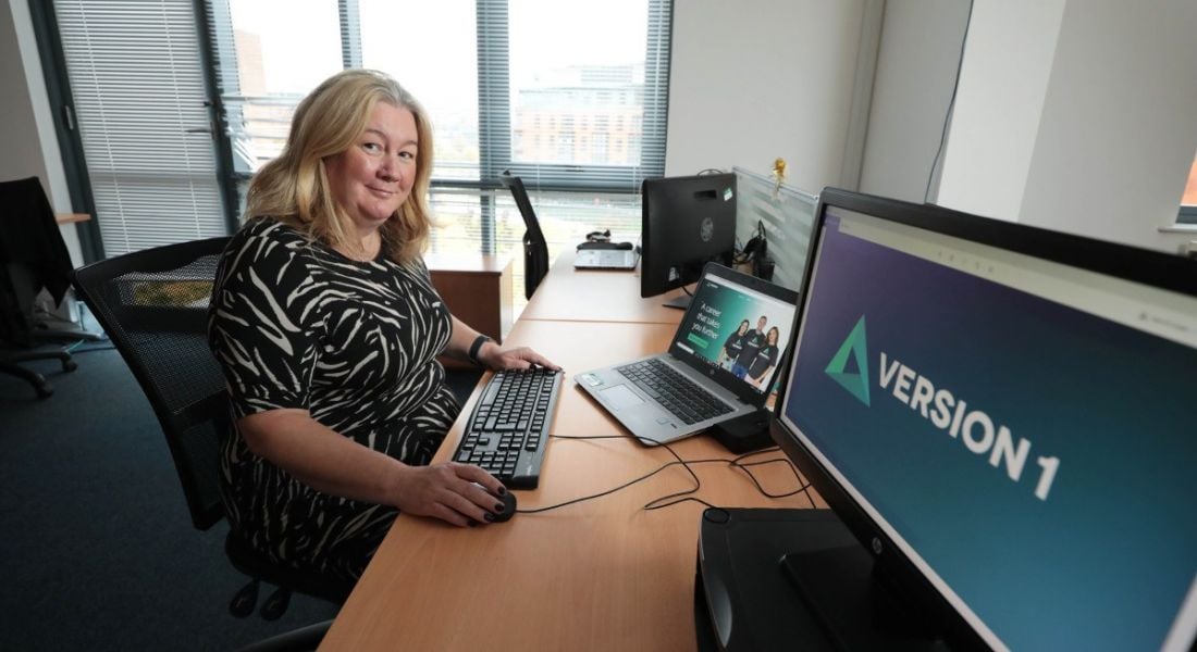Version 1 Northern Ireland director of operations Lorna McAdoo is sitting at a desk in front of a computer with the company logo on the screen.