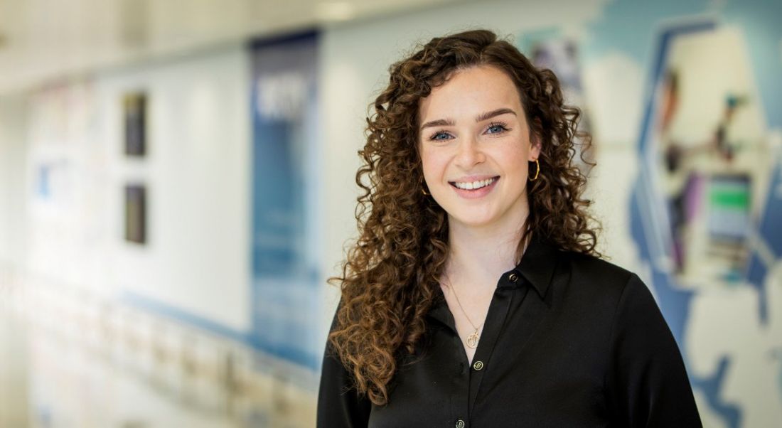 Veronica Boomsma of the Amgen graduate programme is standing in a hallway at the company and smiling into the camera.