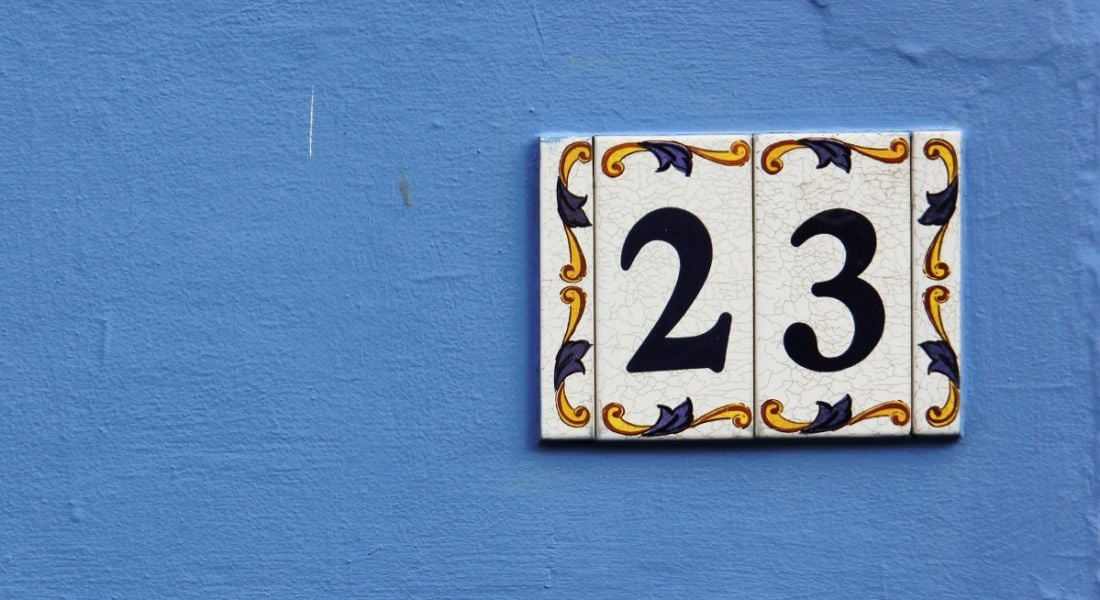 A decorative tile showing the number 23 is placed on a blue painted wall.
