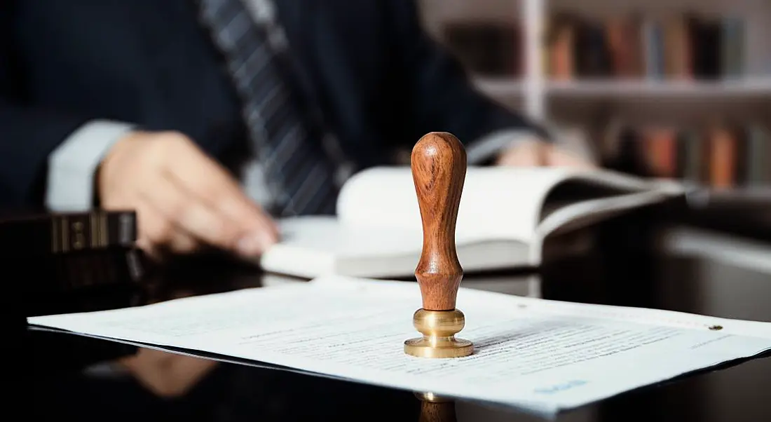 A businessperson is sitting at a desk beside an official letter with a stamp with a wooden handle on it.