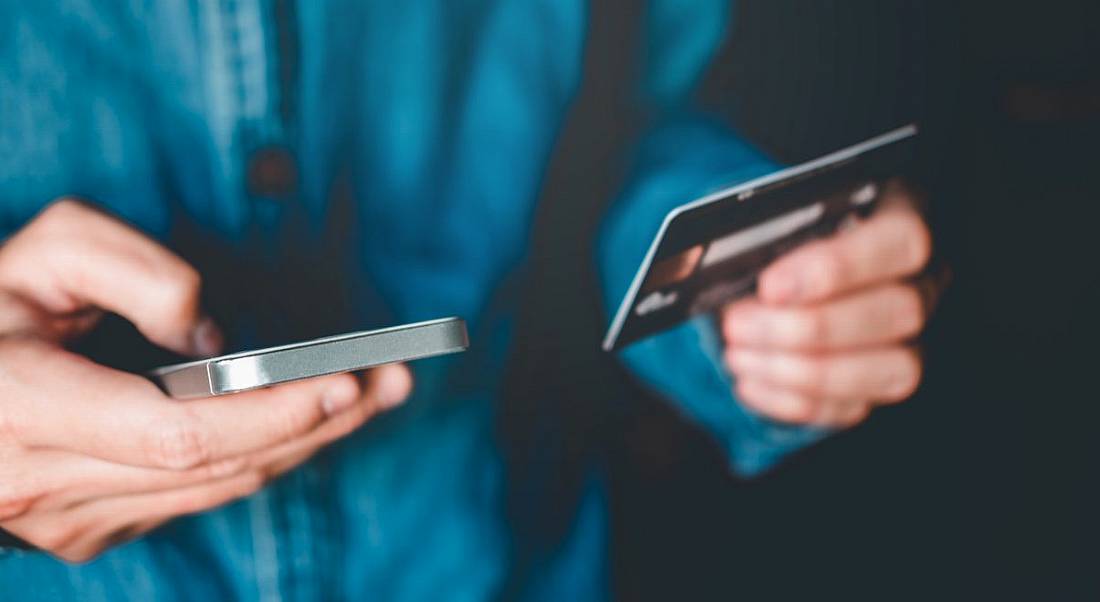 A person is holding a mobile phone in one hand and a bank card in the other against a dark background, symbolising fintech.