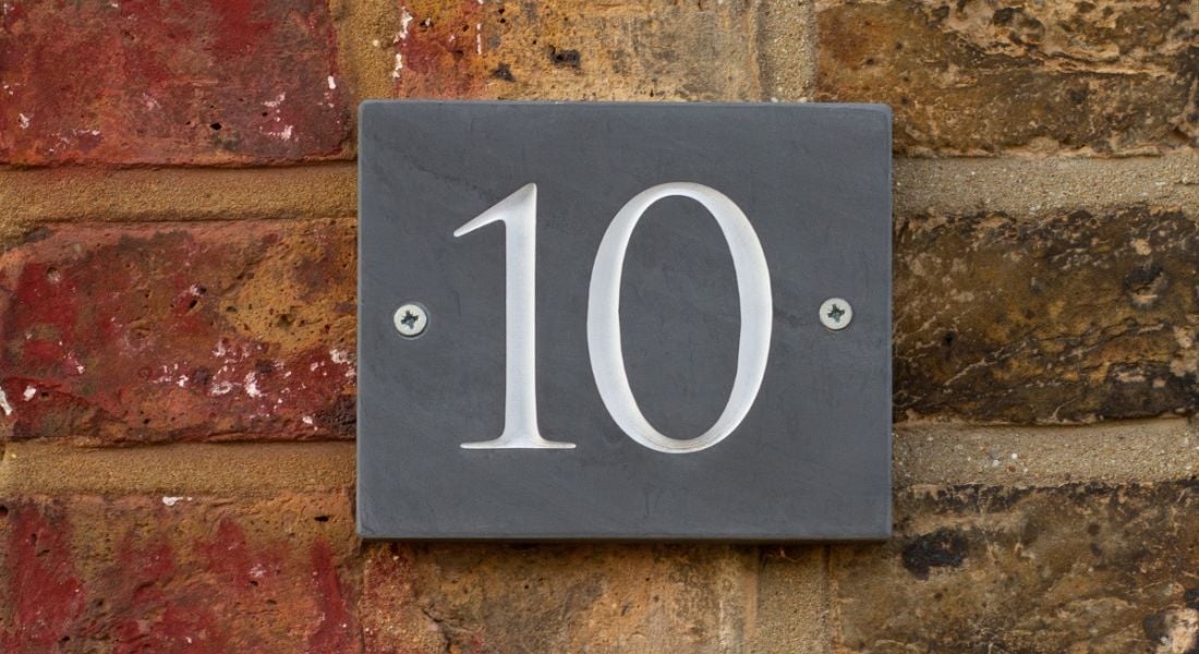 A slate number 10 sign against an old red-brick wall.