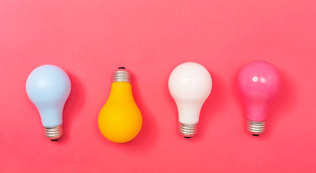 Four multi-coloured lightbulbs against a bright pink background, symbolising work in STEM.