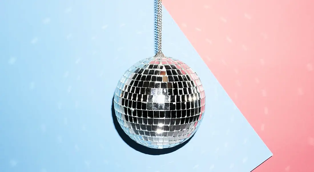 A silver disco ball is hanging against a blue and pink background, symbolising stepping off the dancefloor for self-reflection.