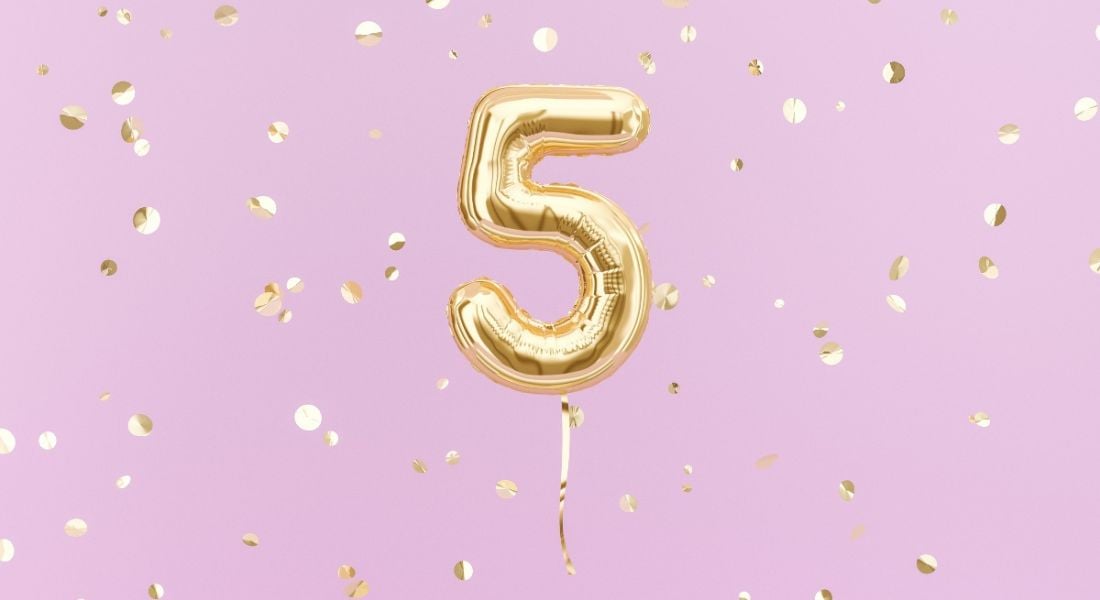 Gold foil balloon in the shape of a number five against a bright pink background.