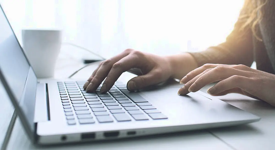 Close-up image of a woman working on a laptop in a sunny room.