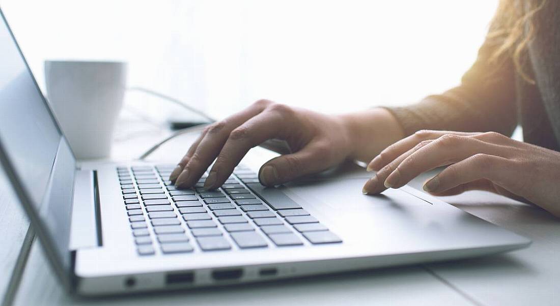 Close-up image of a woman working on a laptop in a sunny room.