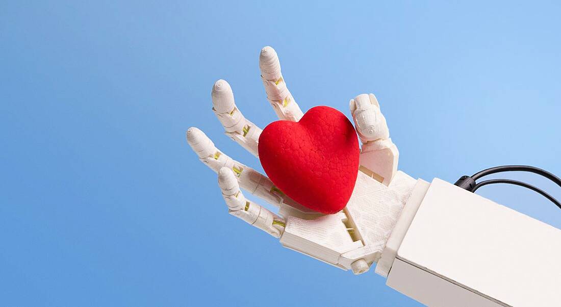 A white robot hand is holding a red heart against a blue background.