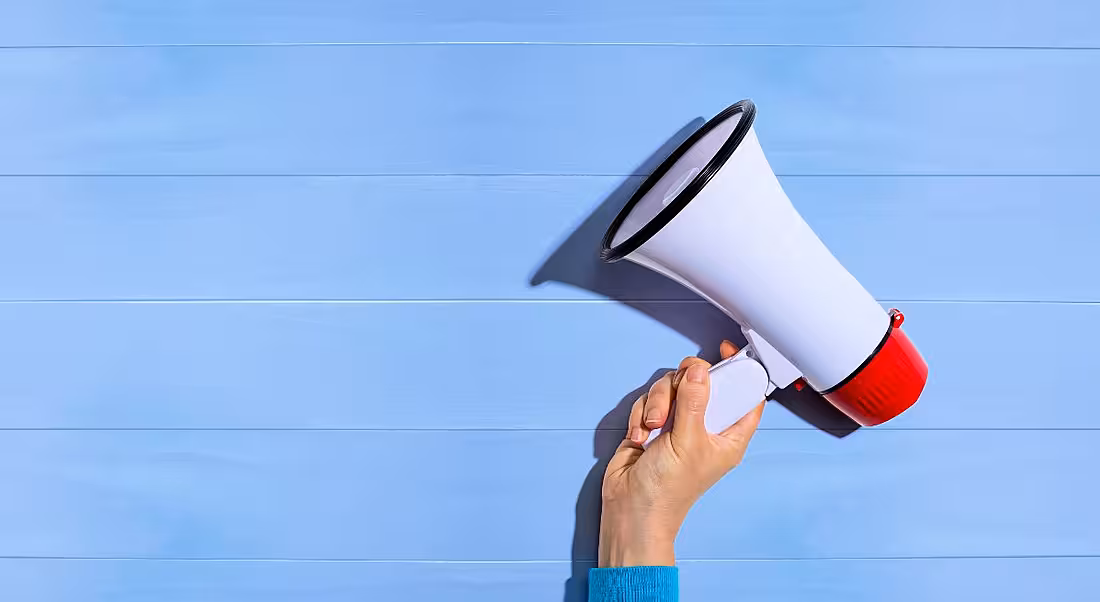 A hand is holding a megaphone up against a pale blue background.