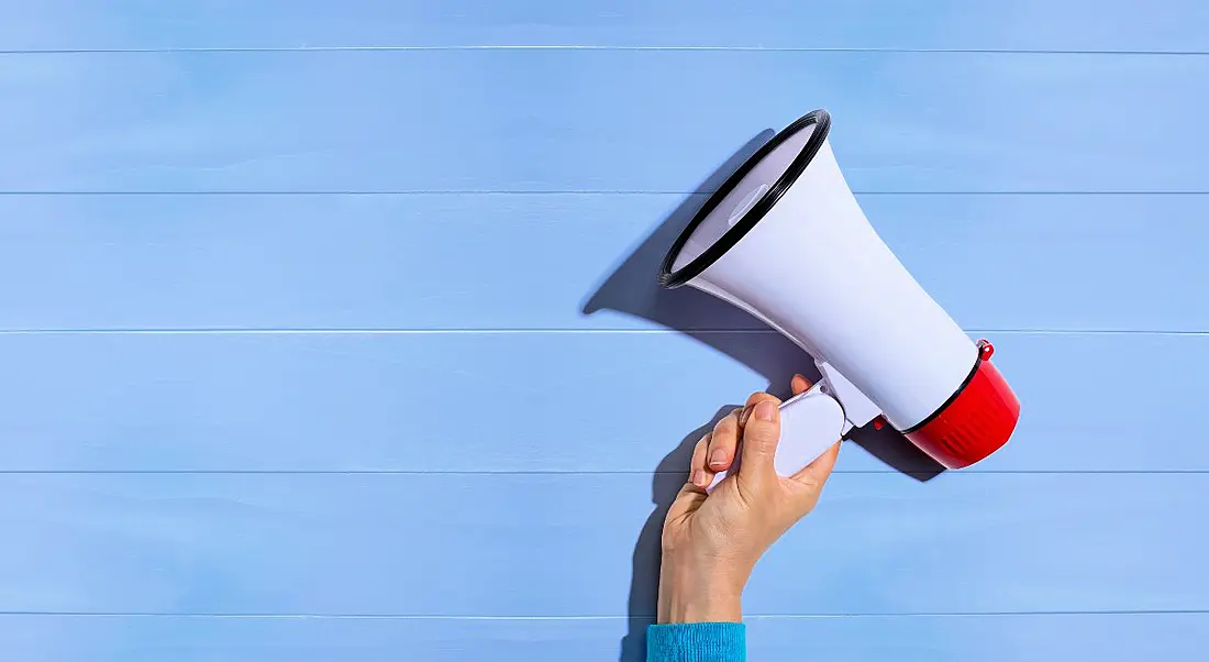 A hand is holding a megaphone up against a pale blue background.