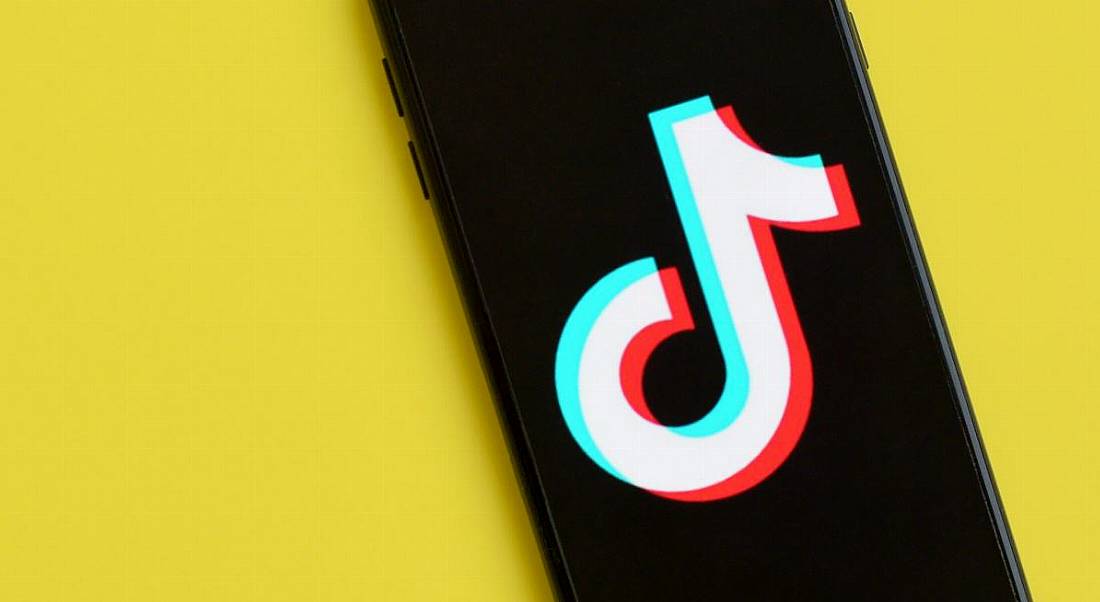 A phone displaying the TikTok logo on a sunny yellow background.