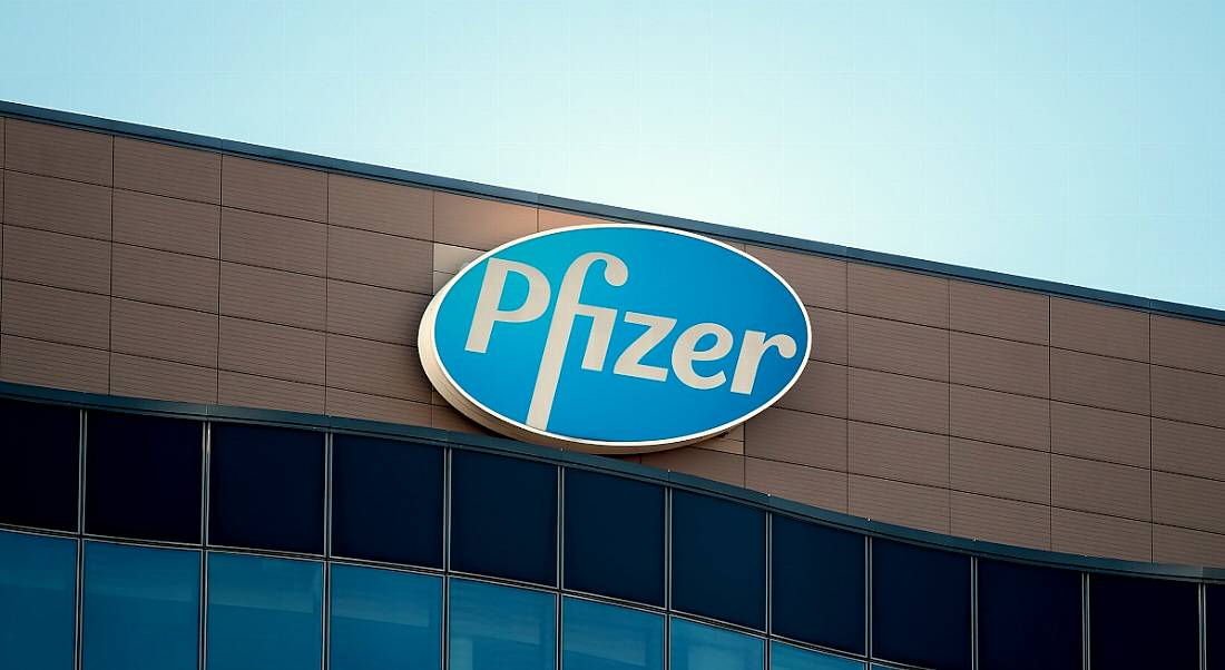 The blue and white Pfizer logo at the top of an office building against a clear, blue sky.